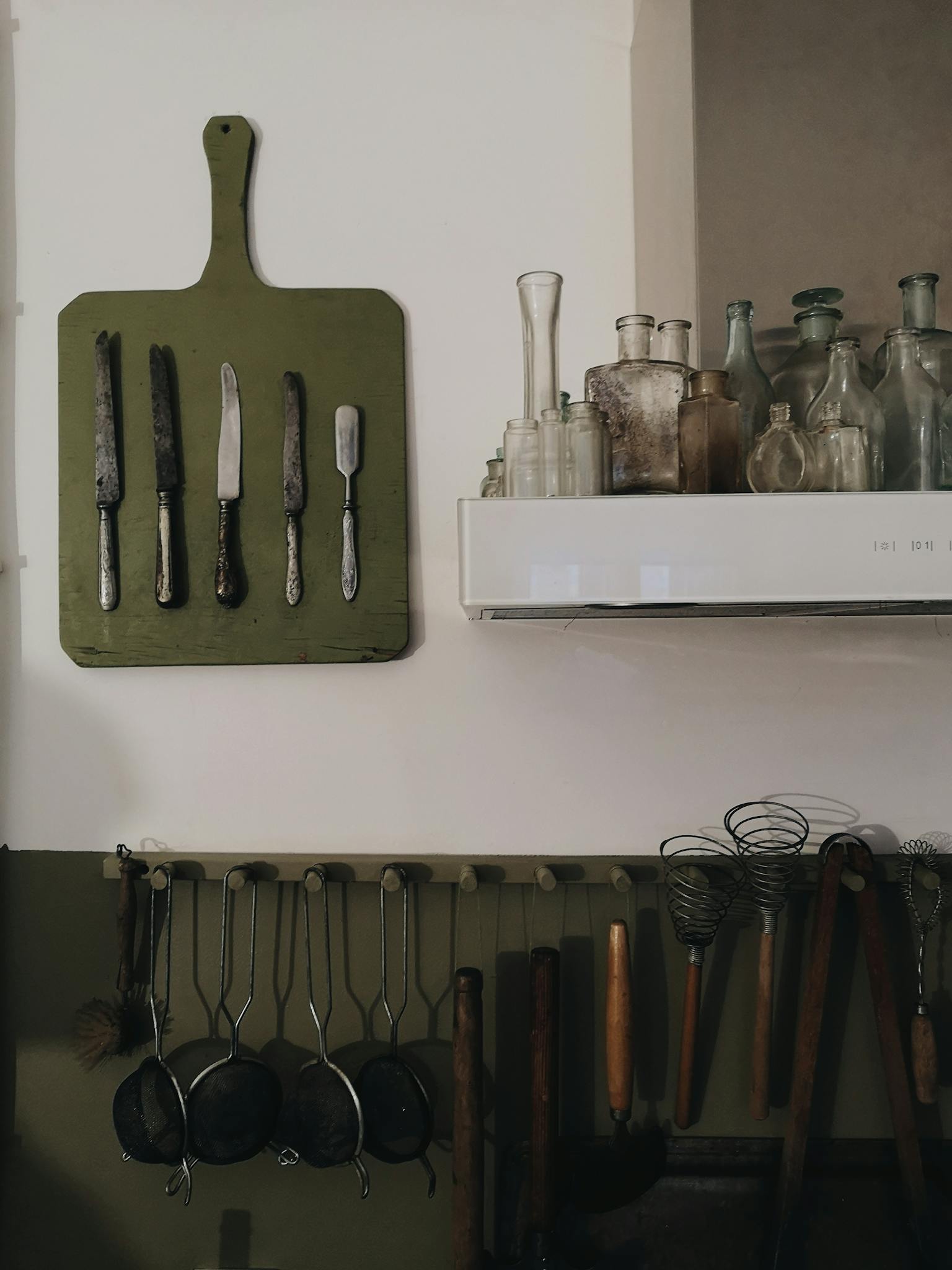 A charming kitchen display featuring vintage knives, utensils, and antique glass bottles for a rustic ambiance.