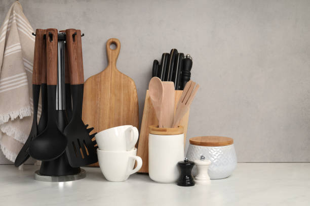 Set of different kitchen utensils and cups on white near gray wall